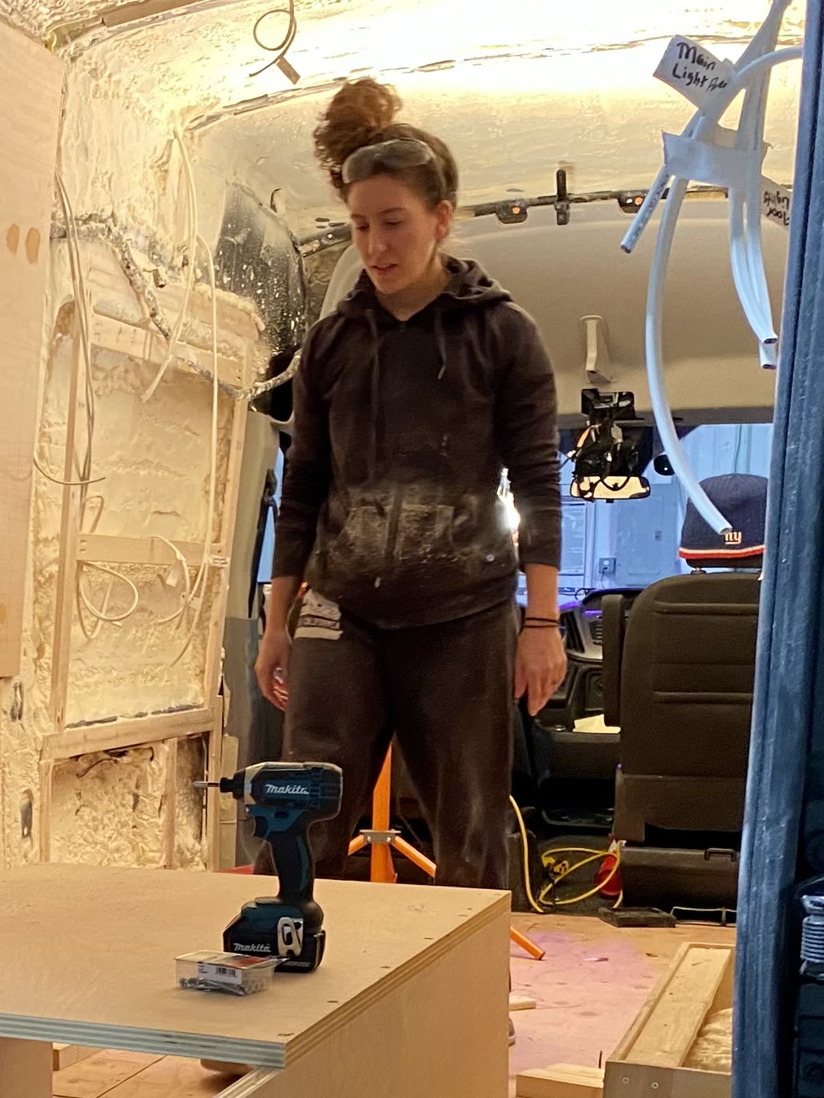 Cristina standing inside the half-built van beside new plywood bench boxes